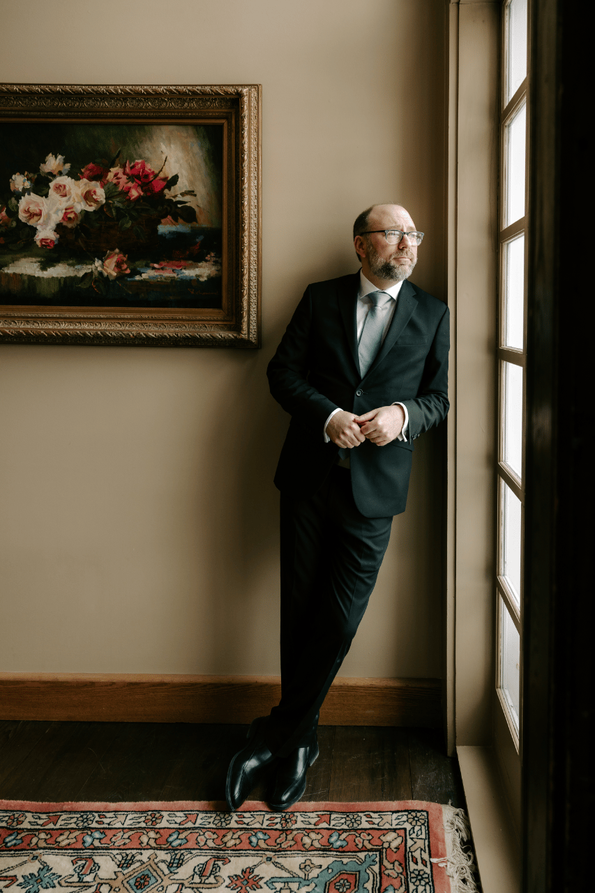 Groom waiting by the window inside the historic inn before their winter ceremony.