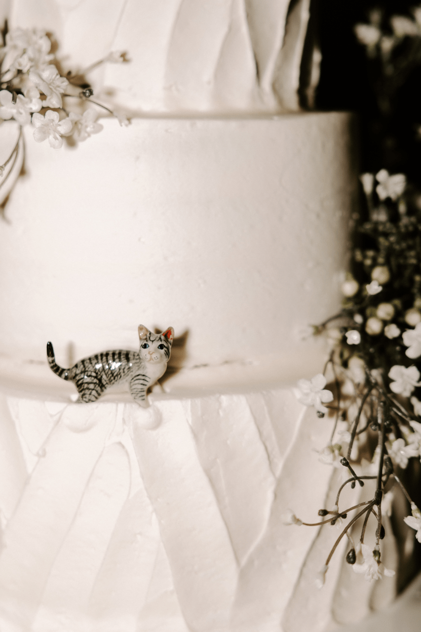 Classic white wedding cake with delicate florals and a whimsical cat figurine topper.